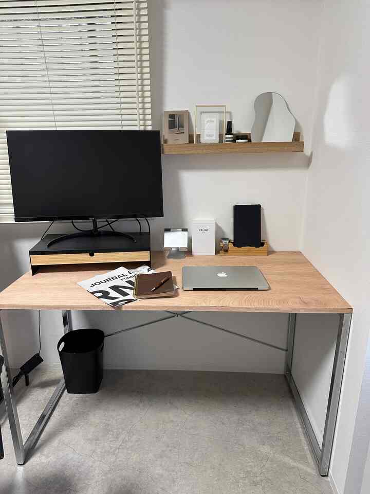 ナチュラルな木目調と白を基調とした寝室の、シンプルなデスクとモニター台が配置されたホームオフィスのある印象的な空間