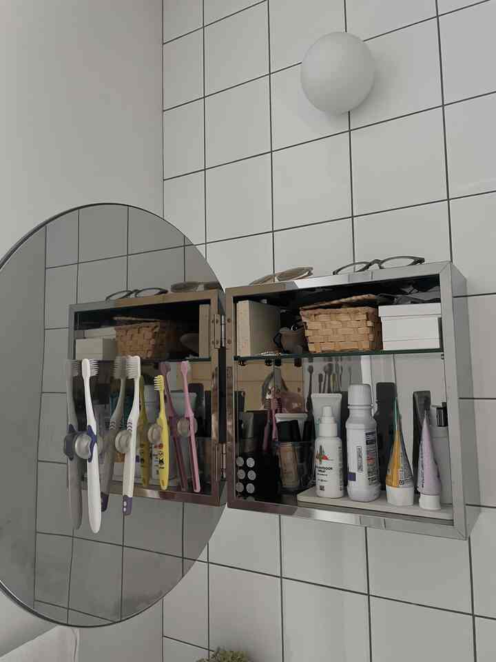 白いタイル壁に設置された丸い鏡と収納可能な鏡台が配置されたバスルームのインテリア