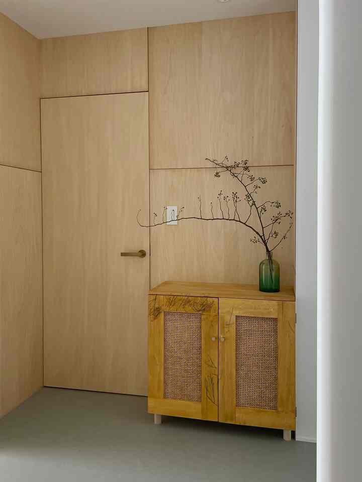 木目調の壁と扉、落書きのあるキャビネットと枝を飾ったシンプルで自然な玄関スペース