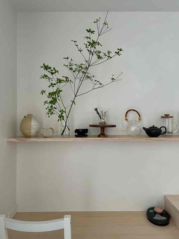 白い壁と木目調の棚があるキッチンのワークスペース、ティーポットやキッチン用品が自然な雰囲気で配置された印象的な空間