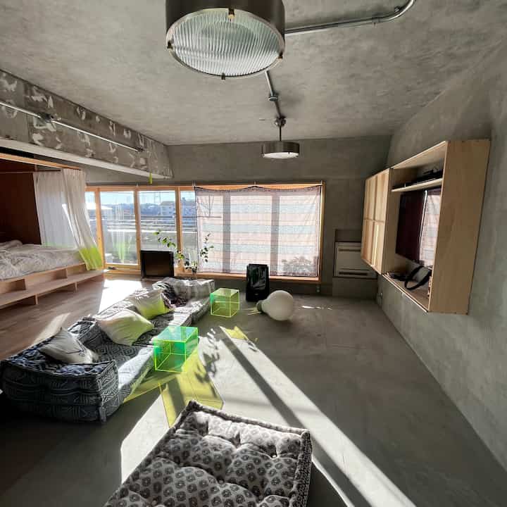 ナチュラルな木目調とネイビーのソファが印象的なモダンなワンルームのリビング、明るいベランダと柔軟なレイアウトが魅力的な空間