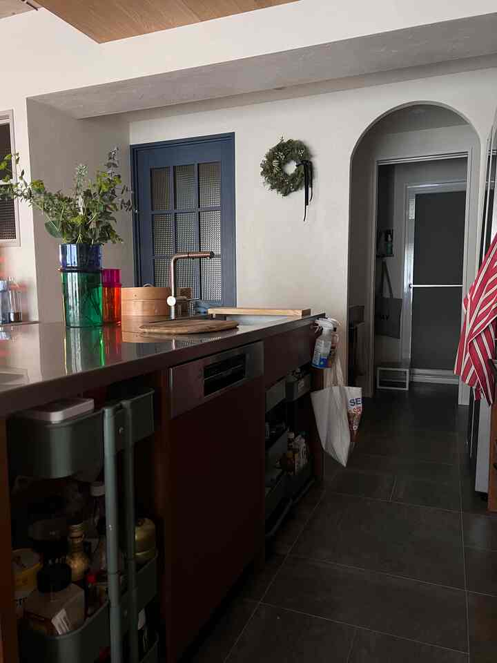 グレーの床とネイビーの扉が印象的なキッチン、木目調のキャビネットとキッチンワゴン、花瓶が配置された温かみのあるインテリア