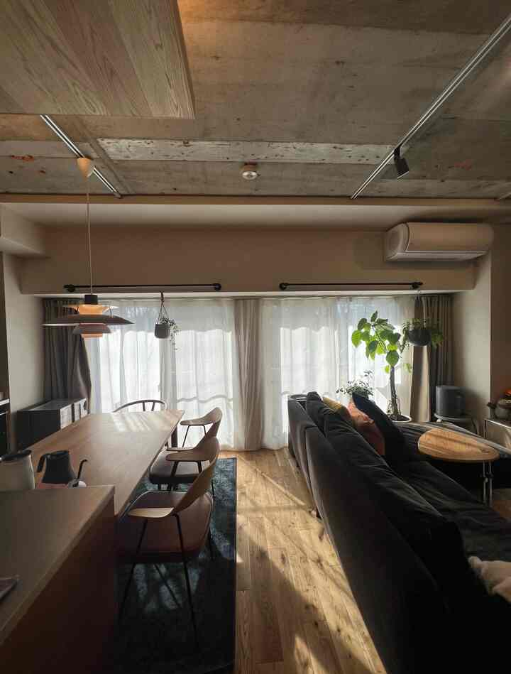 ナチュラルな木目調とネイビーのソファが調和した二人暮らしの寝室とダイニングスペース、温かい自然光が印象的なモダンなインテリア