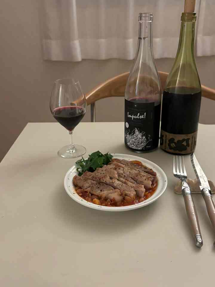 ライトグレー調のダイニングテーブルにワイングラスとカトラリー、肉料理の皿が置かれたモダンで清潔感のあるインテリア