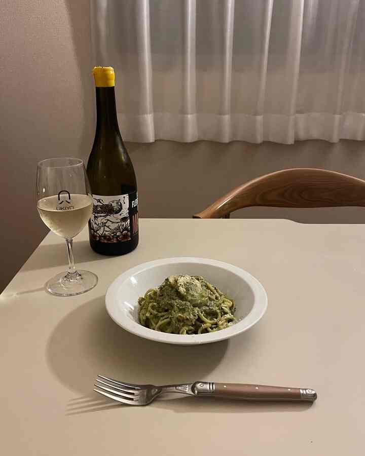 ベージュと白色調のキッチンダイニングテーブル、ワインボトルとワイングラス、パスタの皿が配置された雰囲気のある食事空間