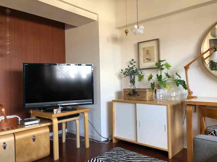 白い壁と木目調の家具が調和するナチュラルスタイルのリビング、テレビ台と植物が配置された雰囲気のあるインテリア