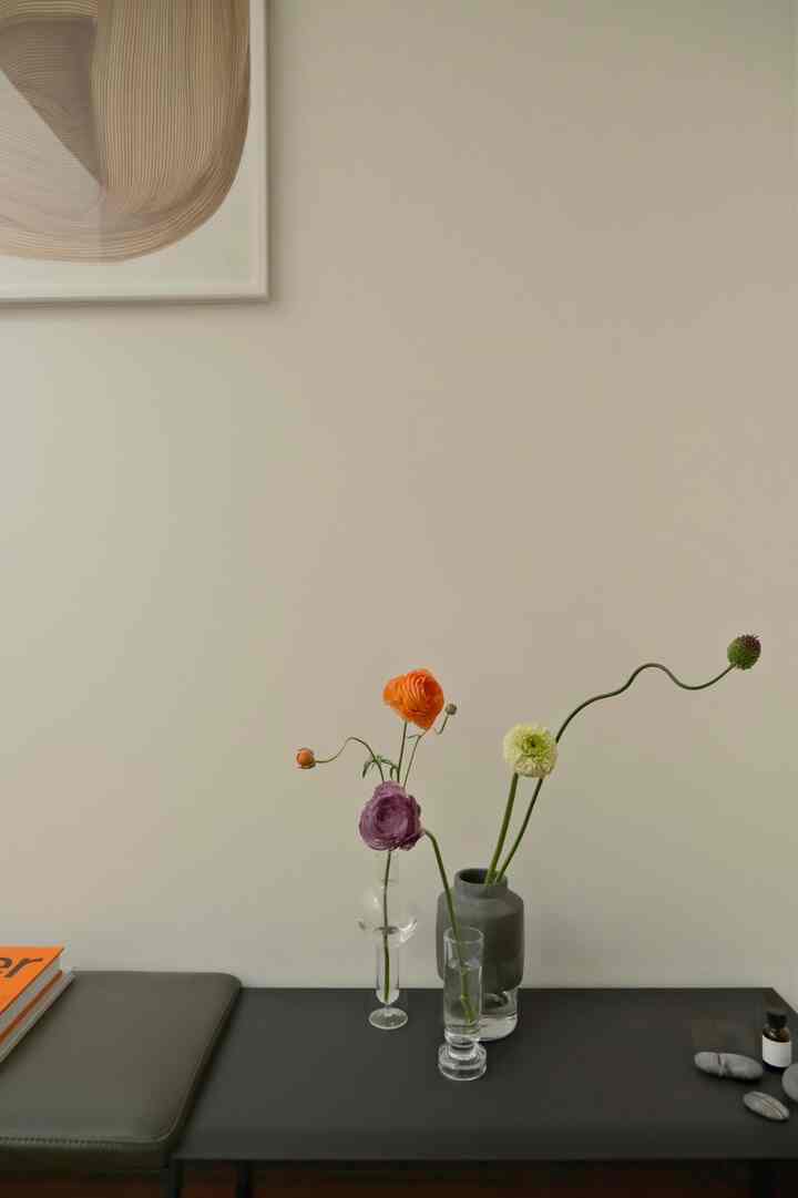 ベージュの壁が印象的な玄関、三つの花瓶に色とりどりの花が配置されたシンプルで落ち着いたインテリア