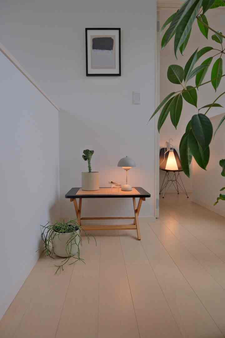 白と木目調の2階ホール、ポータブルライトを置いた小さなテーブルと多くの観葉植物が配置されたシンプルな空間
