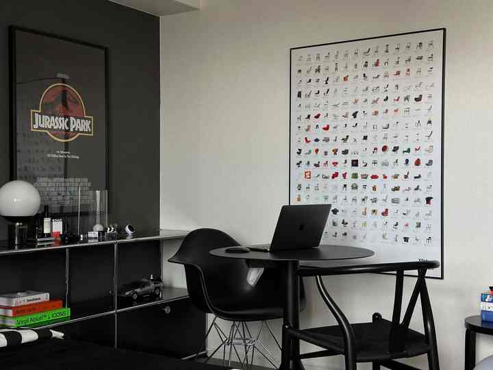 黒を基調とした空間、壁にvitraの椅子コレクションポスターとジュラシックパークのポスターが配置されたモダンなホームオフィス