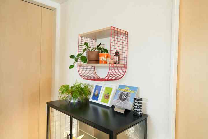 白い壁と天然木のドアが特徴のシンプルな玄関インテリア、黒のキャビネットと赤い棚に植物が配置された清潔感ある空間