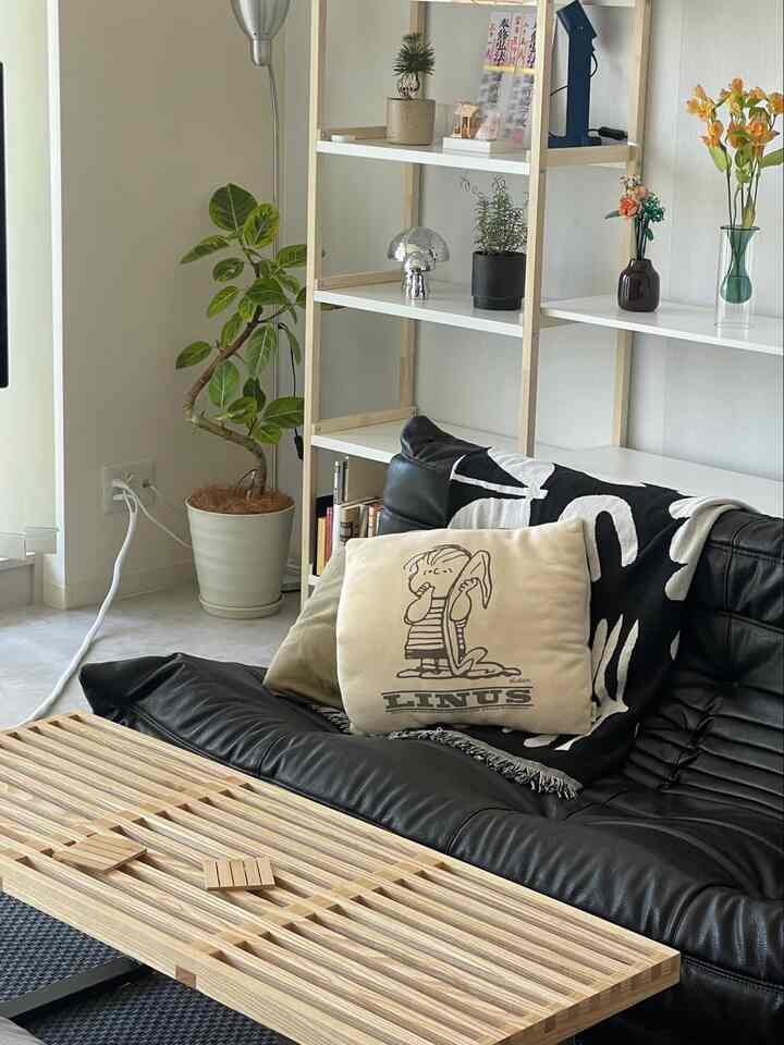 ナチュラルトーンと黒いソファのリビング、木製のテーブルと植物が配置されたシンプルでモダンなインテリア