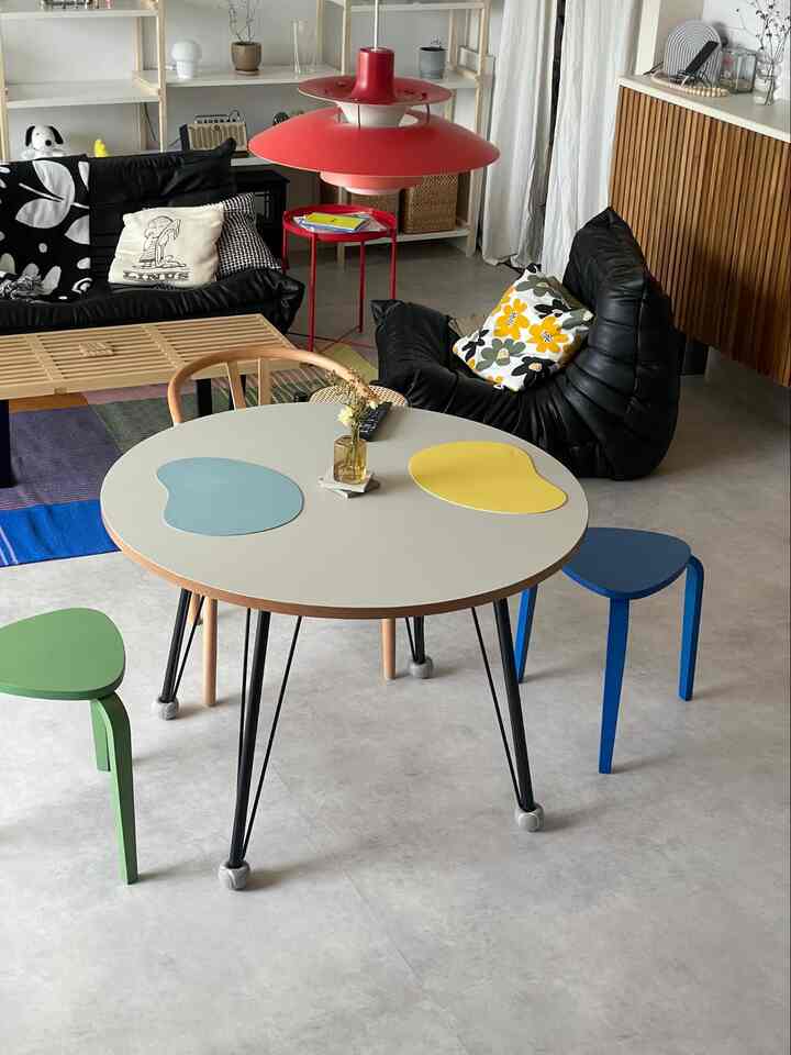 モダンな黒いソファと木目調のスツールがあるダイニングルーム、中央に円形のダイニングテーブルと赤い照明が配置された雰囲気のあるインテリア