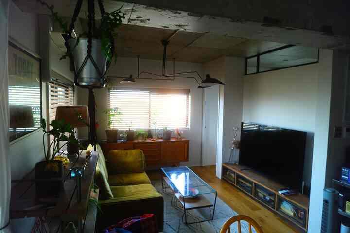 ナチュラルな色調のリビング、オリーブ色のソファとヴィンテージ風サイドボード、窓辺に植物が配置された雰囲気のあるインテリア