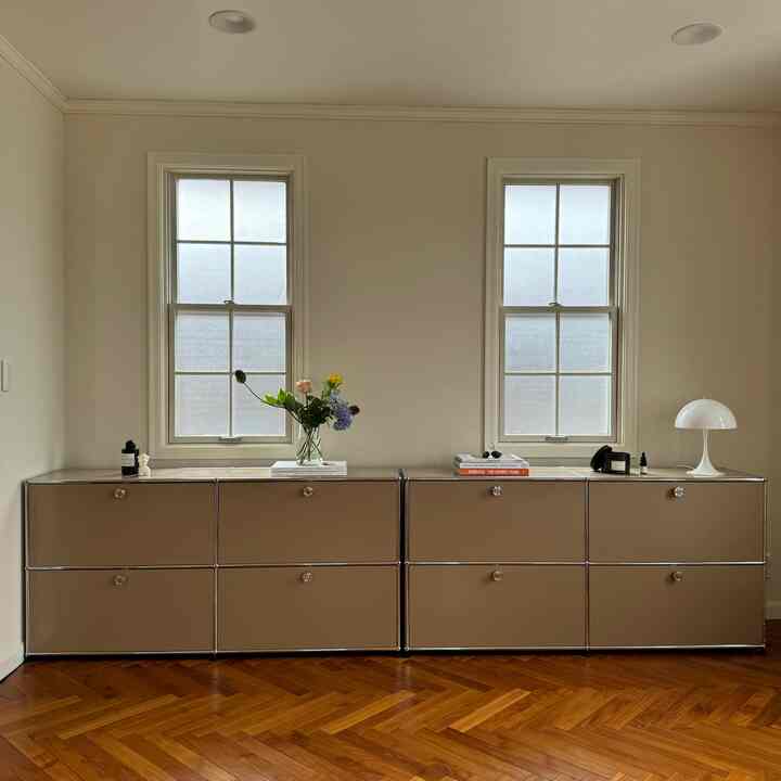 ベージュのUSMハラーキャビネットとテーブルランプが置かれたウッドトーンのフローリングのモダンなリビング