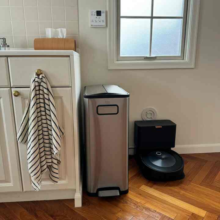 白を基調としたキッチン、ブラウンの木目調床とステンレスのゴミ箱、きれいに掛けられたキッチンタオルが配置された印象的な空間