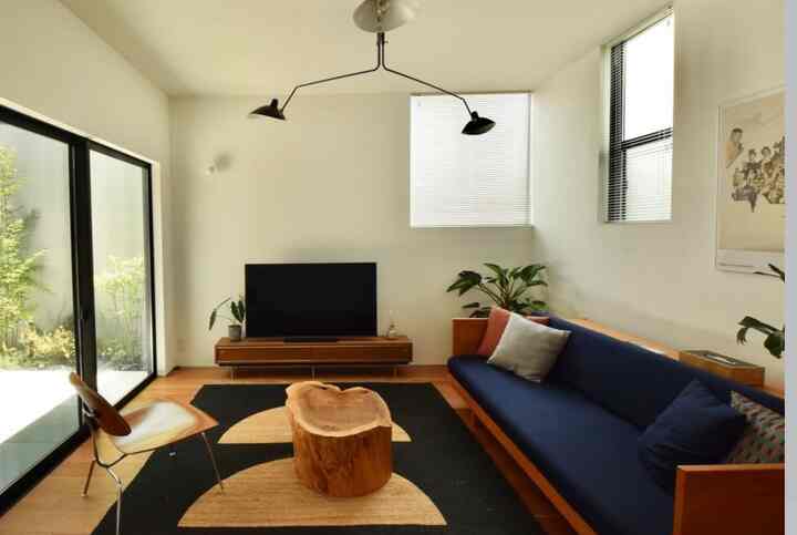 アイボリーの壁とネイビーのソファが配置されたリビング、木製コーヒーテーブルと黒いラグが印象的なナチュラルなミッドセンチュリーモダンインテリア