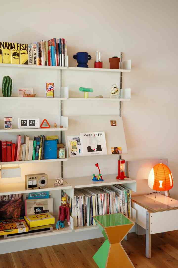 ナチュラルな色調のダイニングルーム、書棚とカラフルなオブジェ、温かみのあるフロアランプが配置された雰囲気のあるインテリア