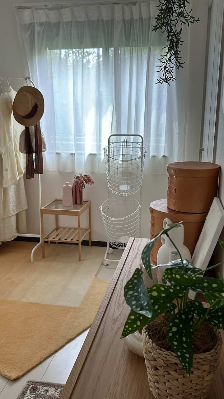 明るいオレンジのラグと白いカーテンがあるナチュラルなドレスルーム、木製家具と整った収納アイテムが配置された雰囲気のあるインテリア