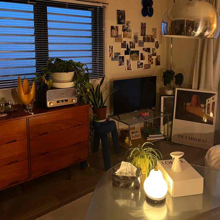 温かみのあるブラウンとホワイトのリビング、木製チェストとフロアランプ、壁に写真アートが配置された雰囲気のある空間