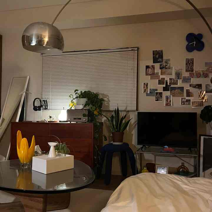 木目調とチャコール色が調和した寝室、木製のチェストや植物、多くのポストカードが壁に飾られた雰囲気のあるインテリア。