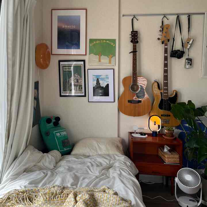 白と茶色の調和がとれた寝室、壁にギターとカメラが配置され、落ち着いた雰囲気のある空間