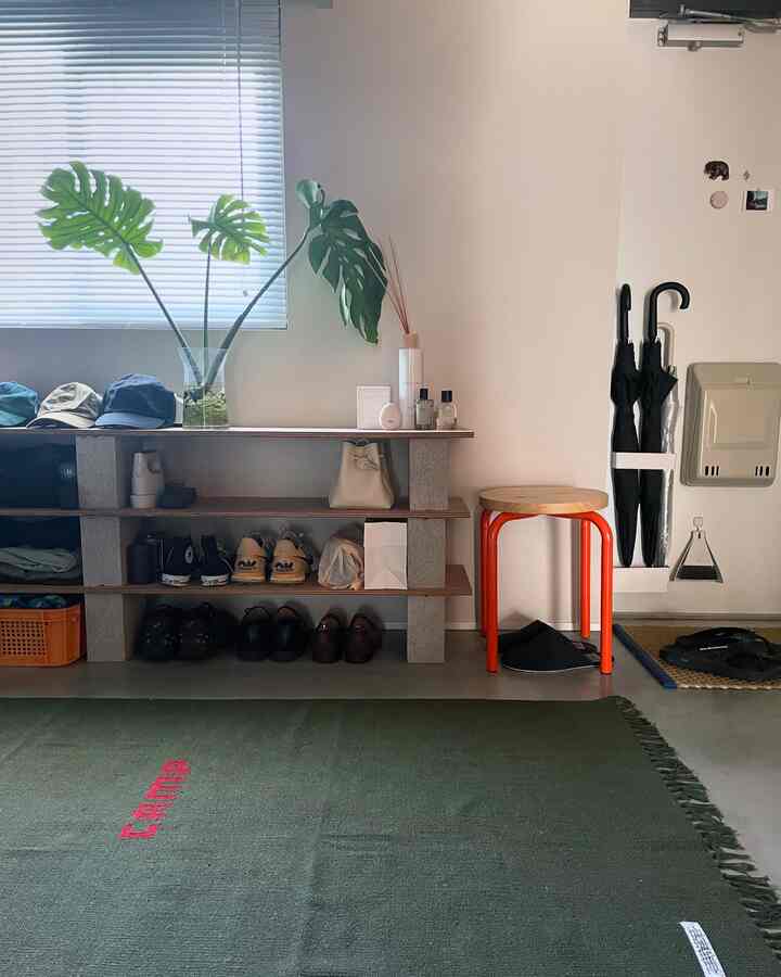 白い壁とグリーンのラグがある玄関、オレンジの脚のスツールと整理された靴棚が配置された清潔で開放感のあるインテリア