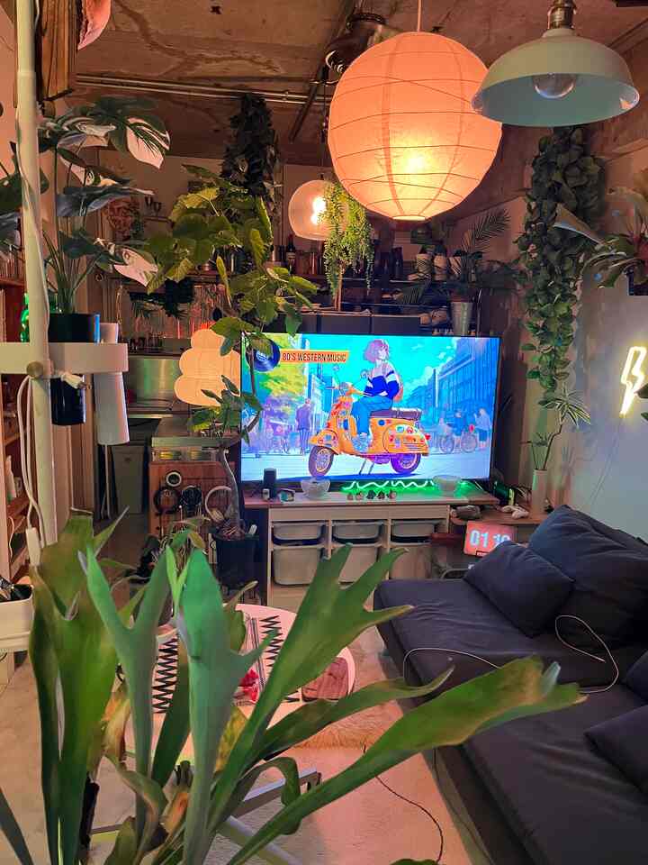 ナチュラルな色調のリビング、黒いソファと白い丸テーブル、豊富な植物が配置された雰囲気のあるインテリア