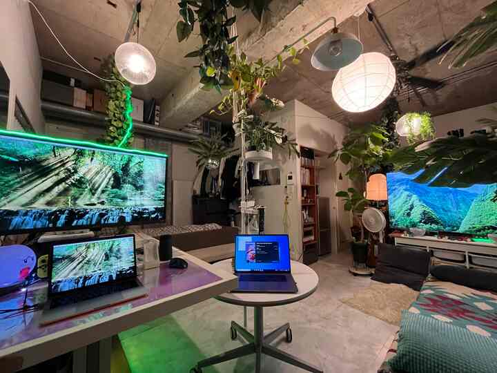 ホワイトトーンの壁と植物が調和したホームオフィス空間、複数のノートパソコンとペンダントライトが配置された雰囲気あるインテリア