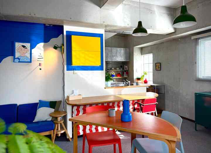 ブルーとイエローがアクセントのナチュラルモダンなリビング兼キッチン空間、木製のダイニングテーブルと赤い椅子が配置された暖かな雰囲気のあるインテリア
