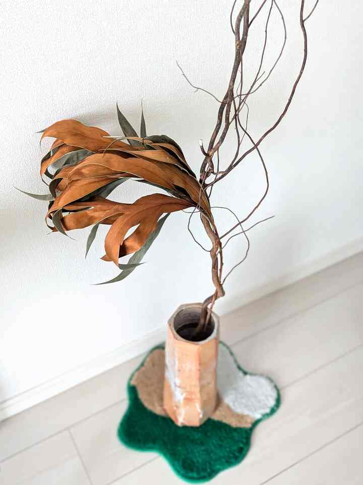 ベージュの壁と床に置かれた花瓶と茶色いドライ植物が調和するナチュラルな雰囲気の空間