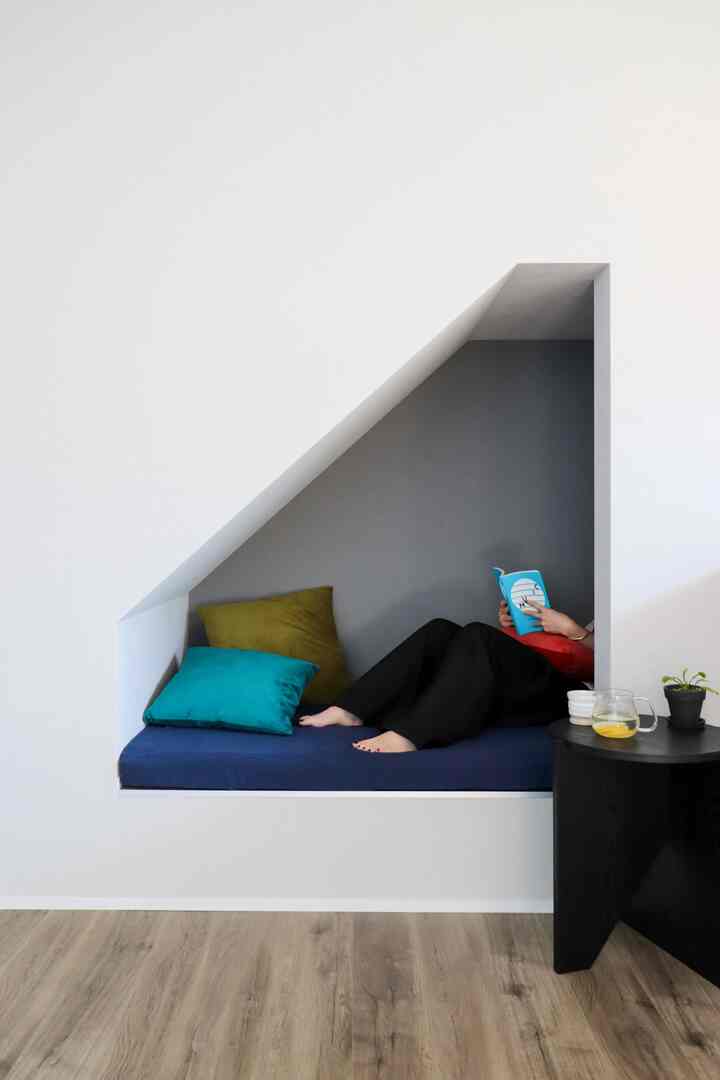 白い壁とナチュラルな木目調の床が特徴のリビングにある居心地の良いヌック、ネイビーマットレスとカラフルなクッションが配置された読書空間