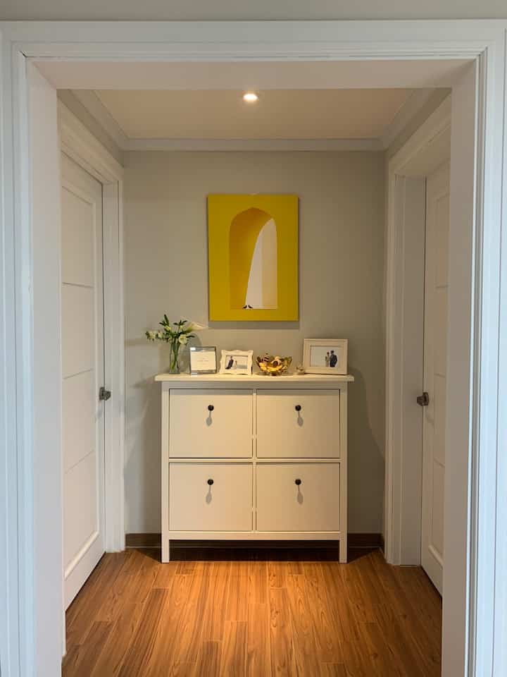 Bright white and wood-tone hallway featuring a yellow framed artwork on the wall, creating a fresh atmosphere