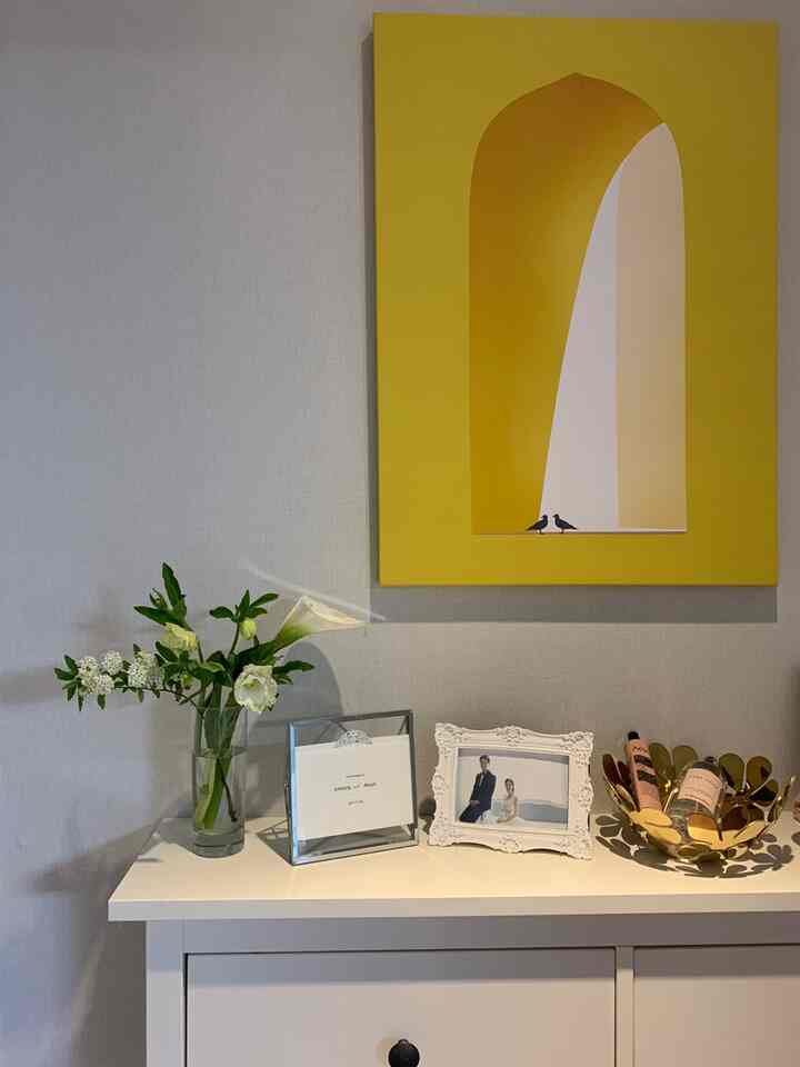 明るい黄色のポスターと白い収納キャビネットに新鮮な花瓶と結婚写真の額が置かれた清潔感のあるインテリア