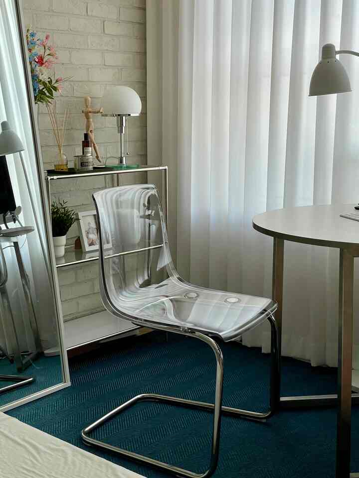 White and metal toned home office featuring a transparent Tobias chair, round desk, and sheer curtains with a modern vibe
