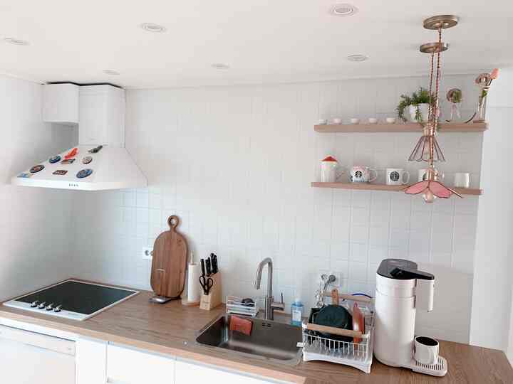 Clean kitchen with white tiled walls and wooden countertops, featuring freestanding shelves and charming pendant lighting for a cozy atmosphere