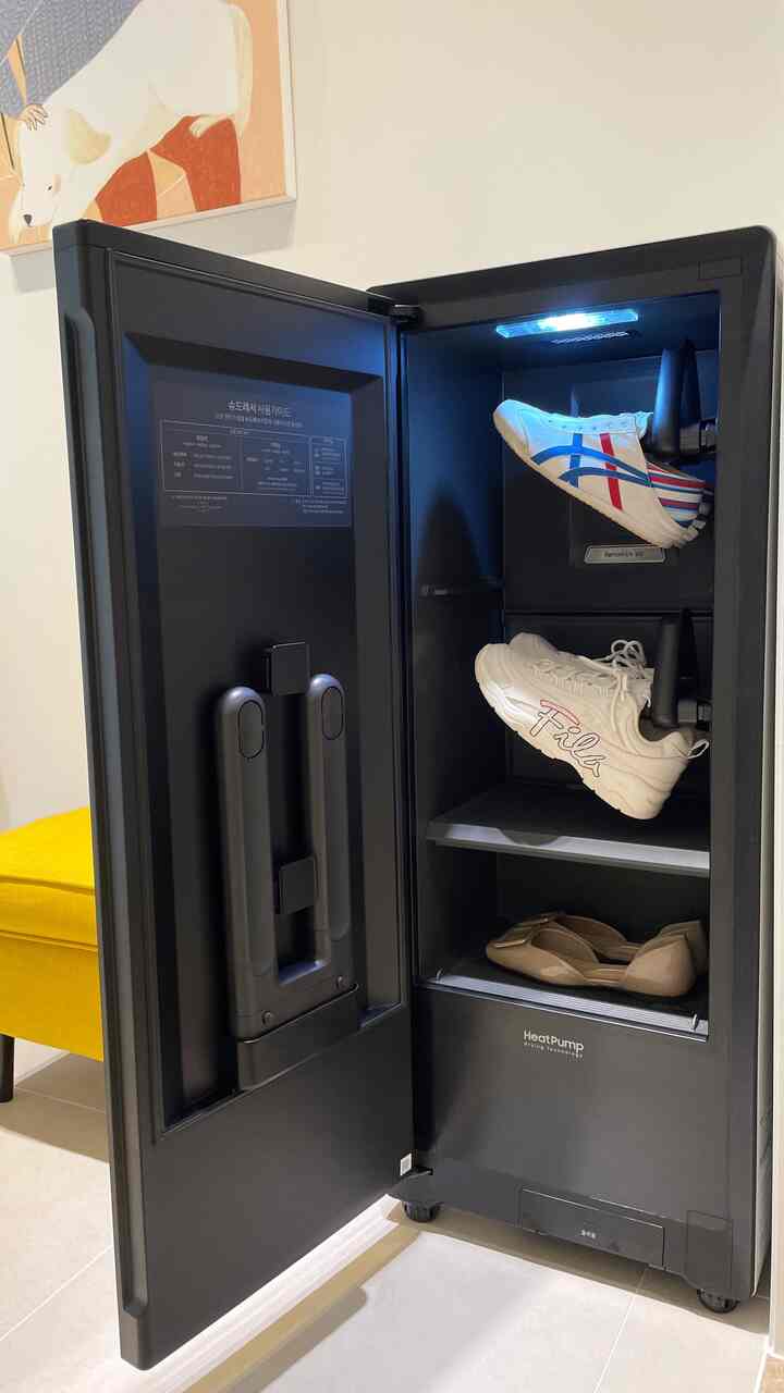 Black shoe care cabinet with white sneakers and beige flats inside, yellow bench visible nearby in a clean setting