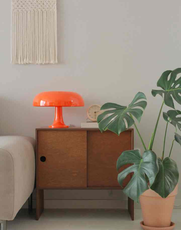 ナチュラルな色調のリビング、ベージュのソファとオレンジのネッシーノテーブルランプ、木製の収納キャビネットが配置された温かみのある空間