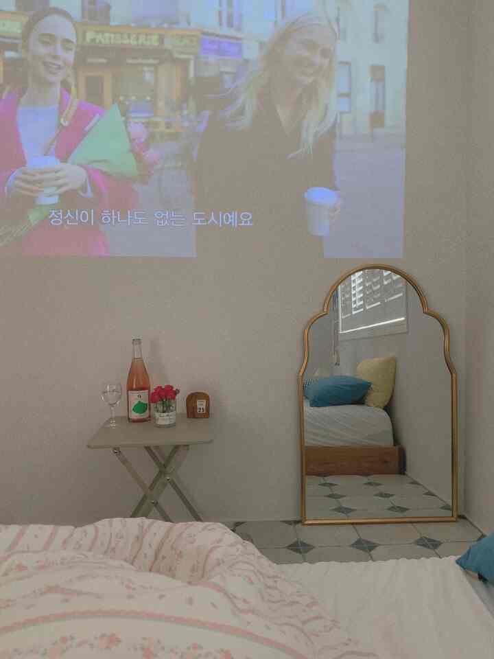 White toned bedroom with bed, gold-framed mirror, and a simple space featuring video projection on the wall