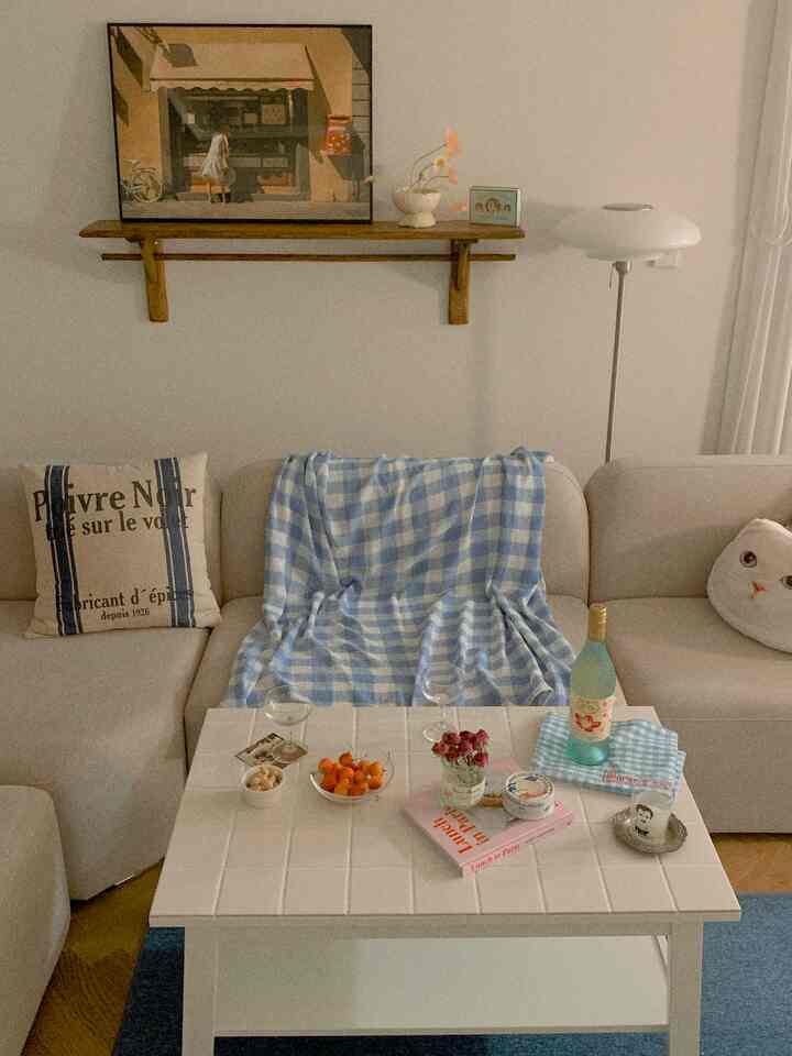 Beige sofa with blue checkered throw in a living room featuring white tiled coffee table and wooden shelf, creating a natural modern ambiance