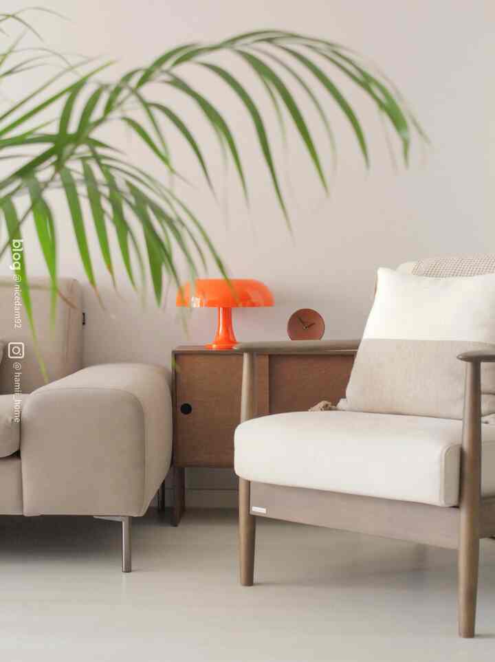 Natural color and wood tone living room featuring beige sofa, wooden armchair, and an orange table lamp as an accent