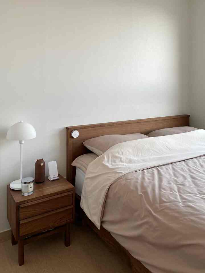 Natural wood-tone bedroom featuring a simple bed and nightstand with a table lamp and candle creating a calm atmosphere
