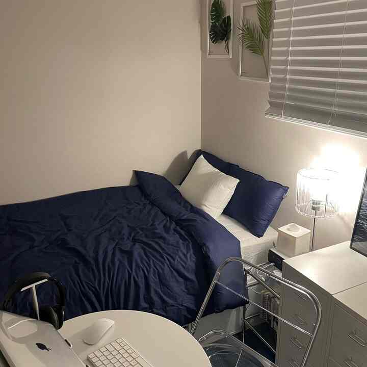 Natural color walls and modern navy bedding in a compact bedroom for single household, featuring a simple desk and floor lamp creating cozy atmosphere