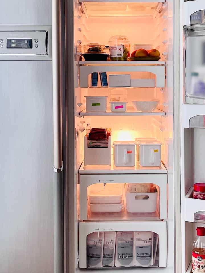 Interior of a refrigerator neatly organized with white storage boxes and bowls under bright white lighting