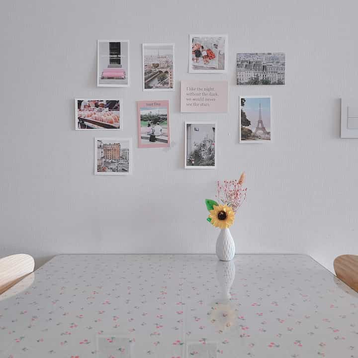 Cozy kitchen space with white walls, pink posters, a two-person dining table covered in floral tablecloth and a sunflower vase centerpiece