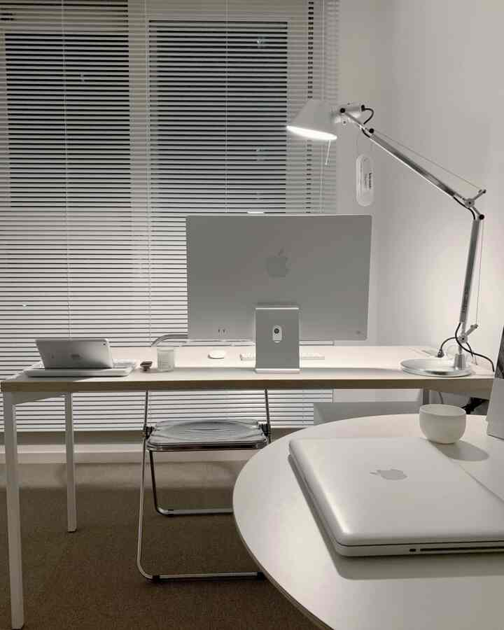 A white and gray toned home office featuring an iMac and a laptop with a simple work environment