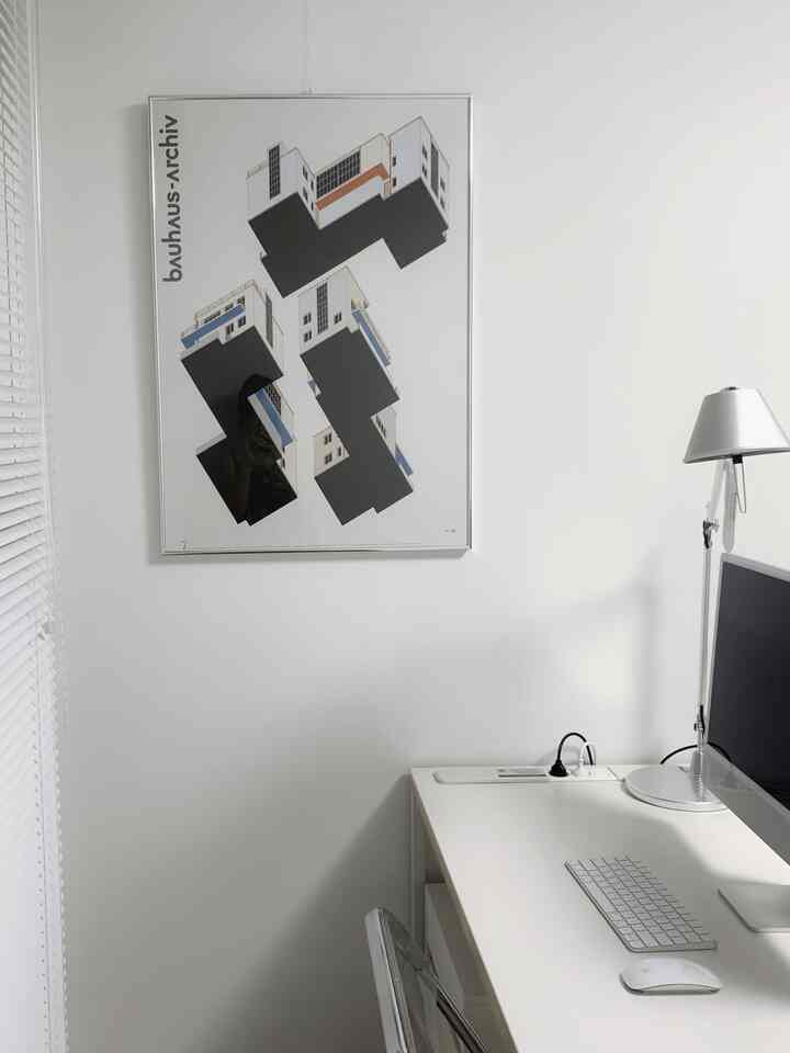 Monotone minimal style home office featuring a white desk and a Bauhaus poster, creating a clean workspace
