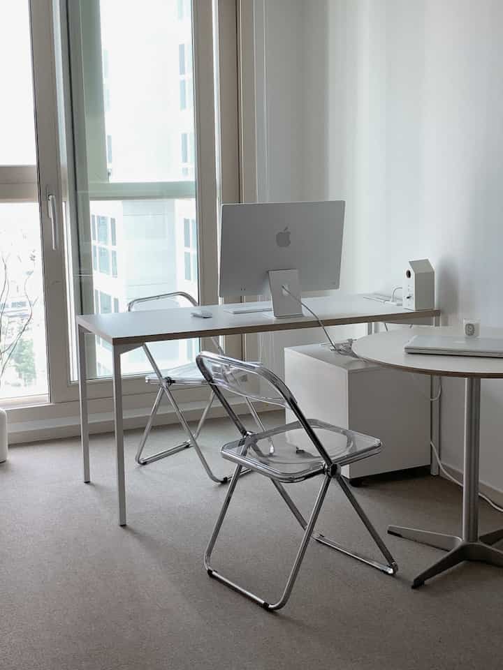 Monotone minimal home office featuring a white desk, transparent chairs, and an iMac computer in a clean workspace