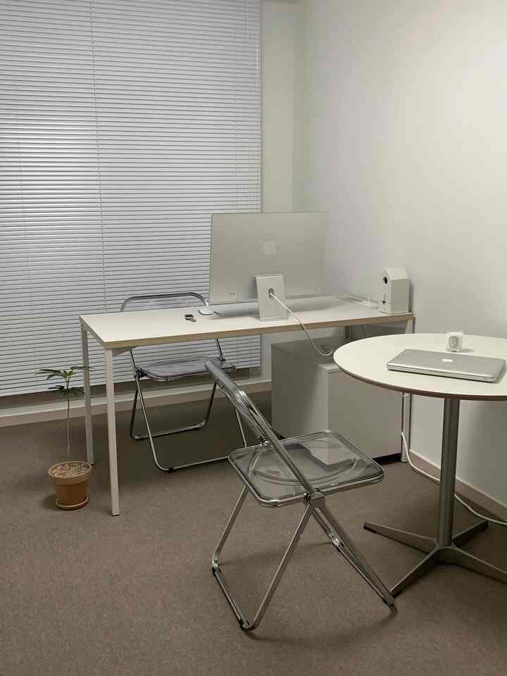 Simple home office with white and brown tones featuring white desks, transparent chairs, and tile carpet flooring creating a calm atmosphere