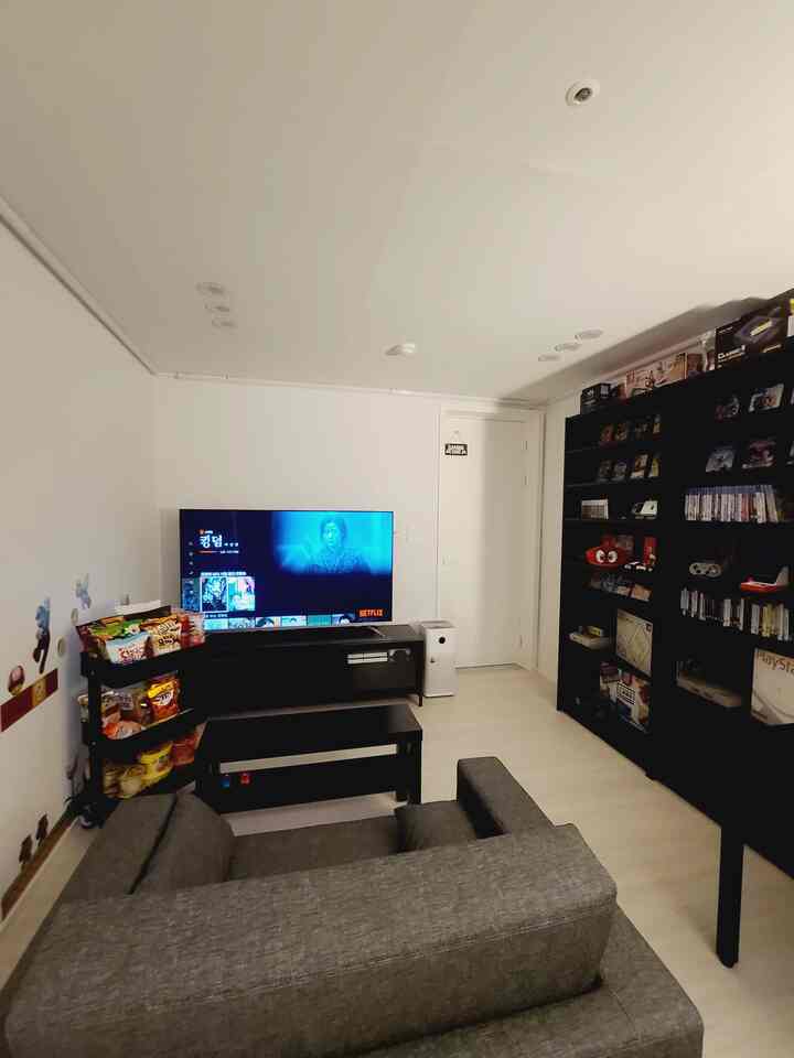 Cozy home cinema room with white walls and ceiling, black furniture, a large gray sofa, and expansive bookshelf