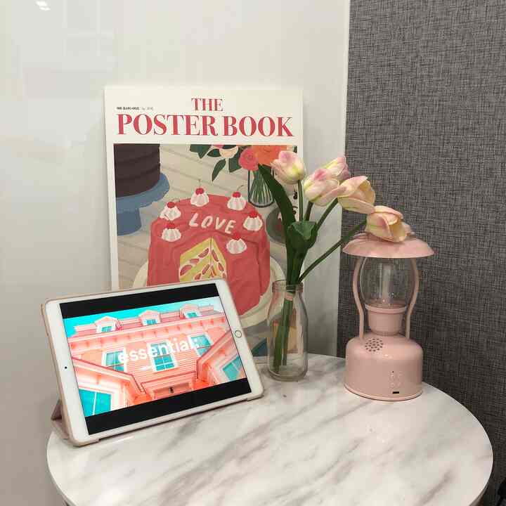 Studio apartment setting with pink accessories and white marble side table featuring an iPad and vase of flowers in a simple interior